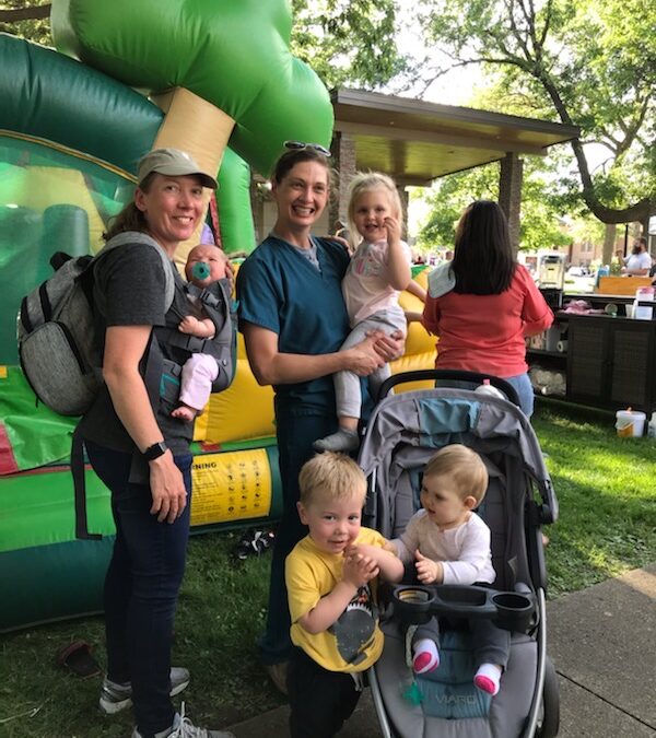 Courtney Brewer (L) and Erin Schwarte (R) smile in front of a bounce house with their happy kids at Produce in the Park June 2022